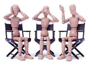 Three wooden dolls sitting doing bodily gestures. Concept of the three wise monkeys.